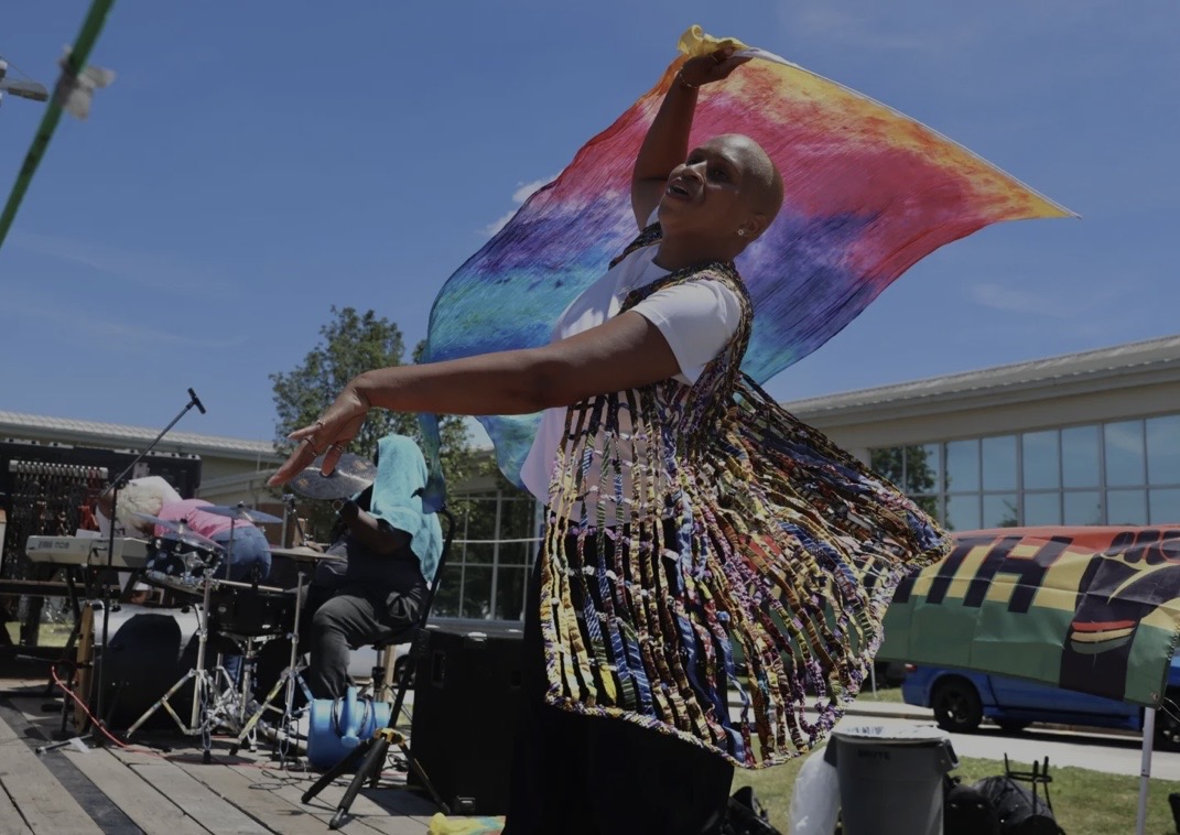 Joy ministering in worship dance outdoors with a colorful hand dyed flag